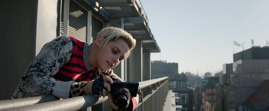 Sabina leans over the railing with her camera as she takes a photo of Elena arriving.