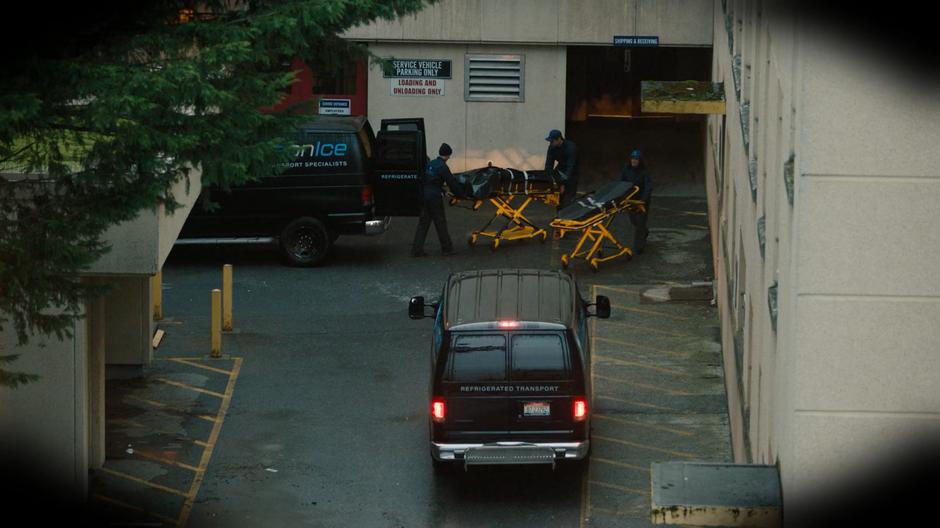 Delivery people unload bodies from refrigerated transport vans.