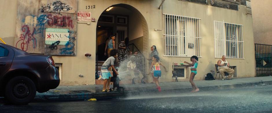 Dinah glances over her shoulder as she walks up the stairs to some kids playing in a hydrant in the street.