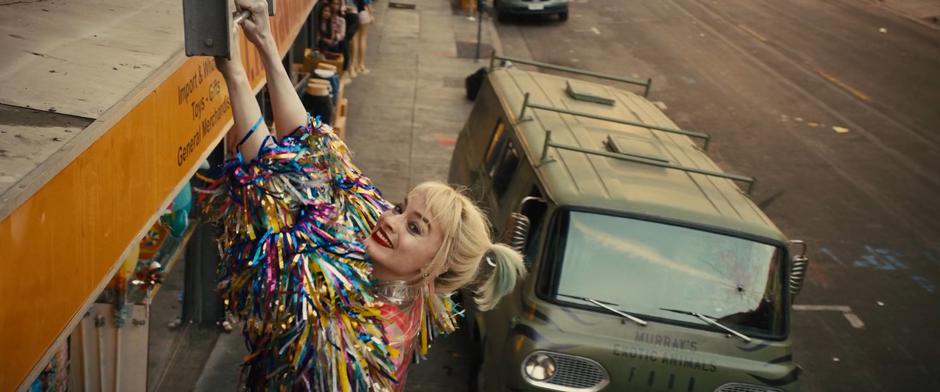 Harley smiles at the camera after leaping up onto the fire escape ladder to avoid being hit by Ralph Murray's van.