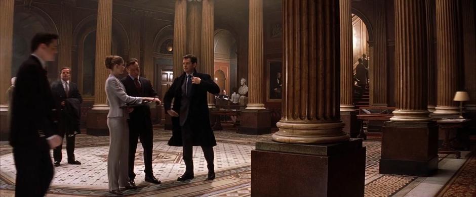 Bond puts on his jacket while talking with Frost and Graves in the ground floor of the lobby.