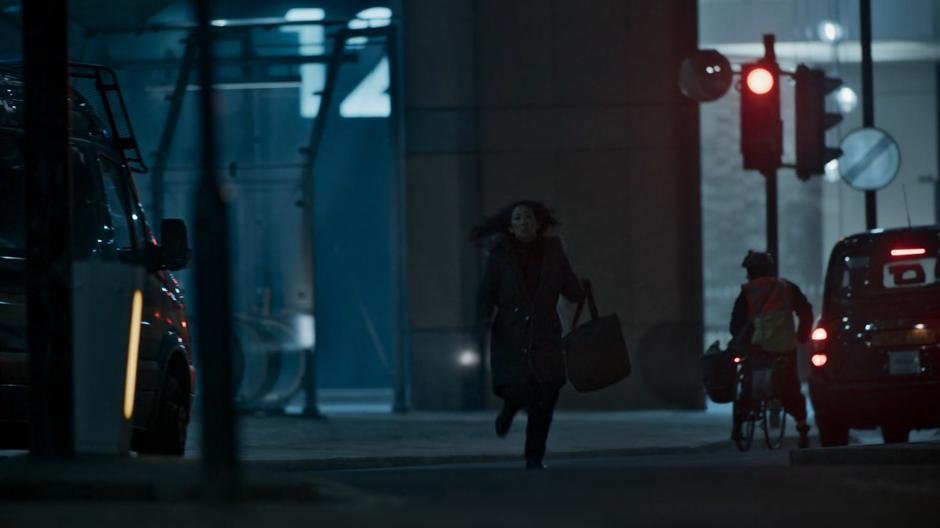 Eve runs across the street holding her bag.