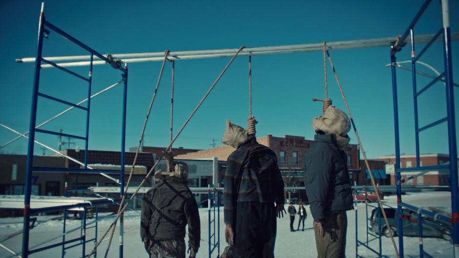 Doc and Wynonna turn to look at three bodies hanging from a scaffolding off the main street.