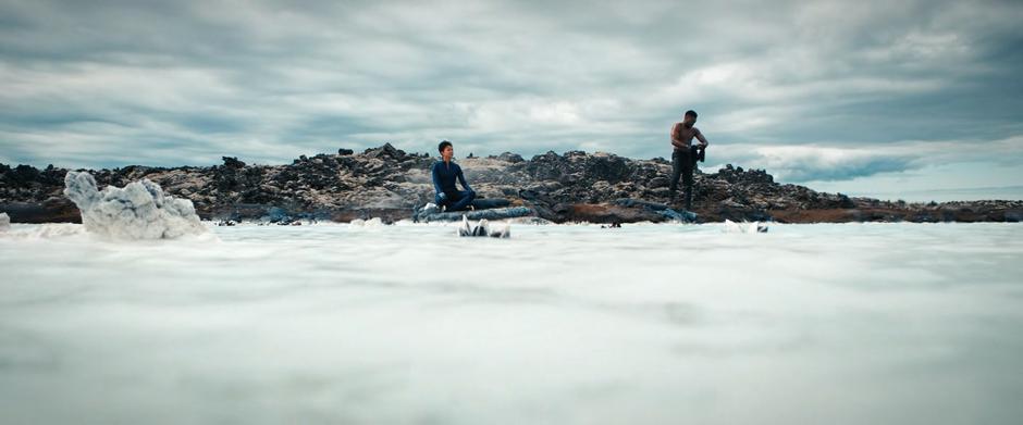 Michael sits on the shore while Booker rings the water out of his shirt.