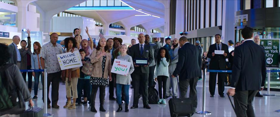 Family members of the students stand with signs waiting to welcome them home.