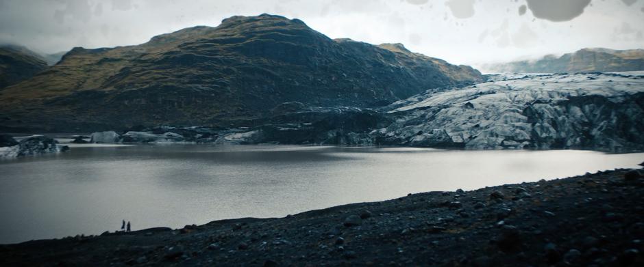 Saru and Tilly walk along the shore beneath the glacier.