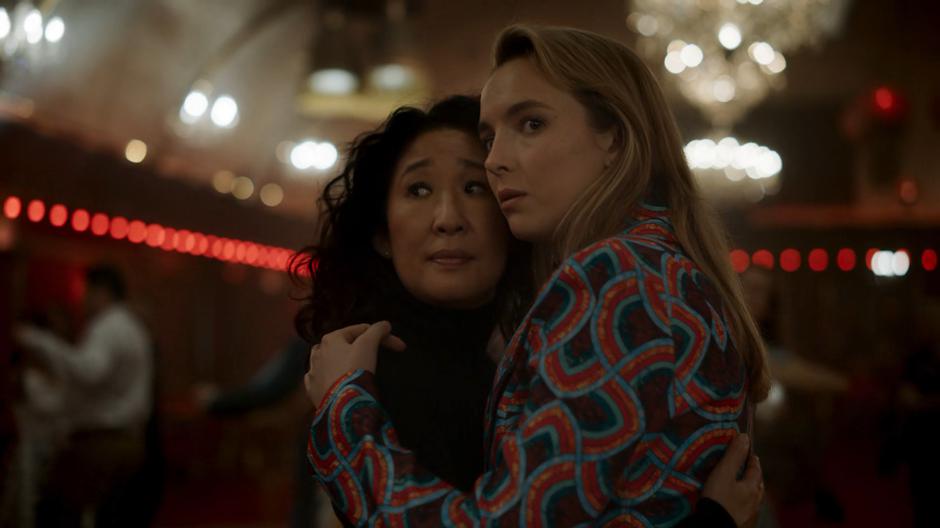 Eve and Villanelle dance close together and look across the dance floor to another dancing couple.