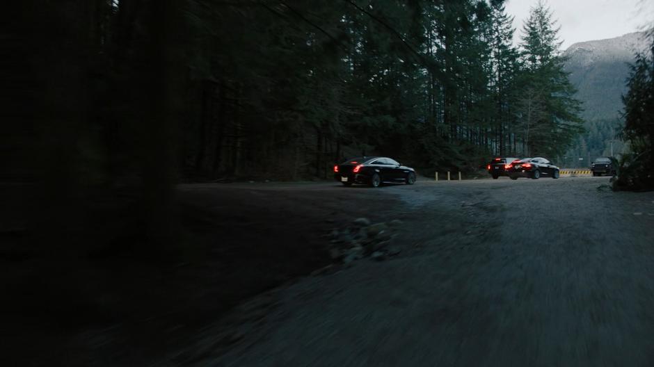 Several cars drive down the dirt road towards the dam.