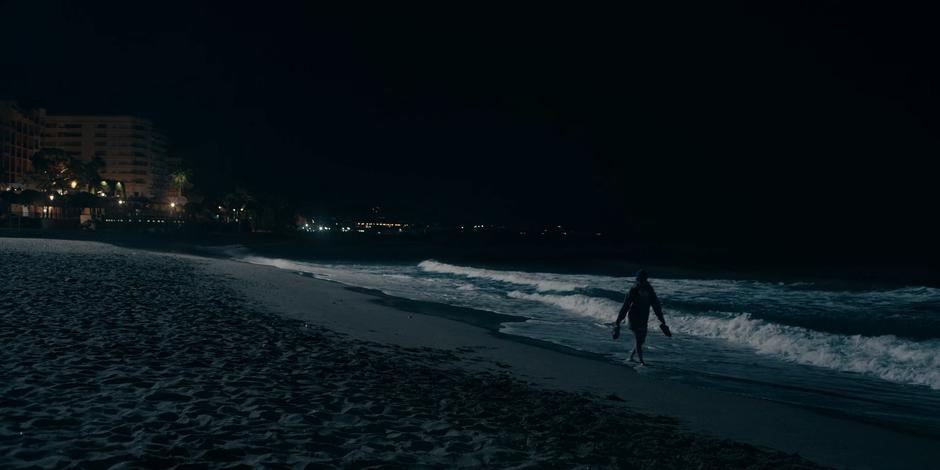 Ava holds her shoes in her hands as she walks through the surf at night.