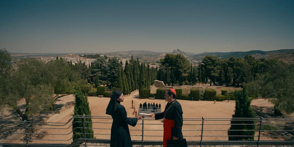 Cardinal Duretti hands Mother Superion an envelope as the nuns train below.