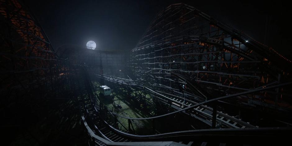 Tommy approaches the back of Ryan's van where it is parked in the middle of a wooden rollercoaster.