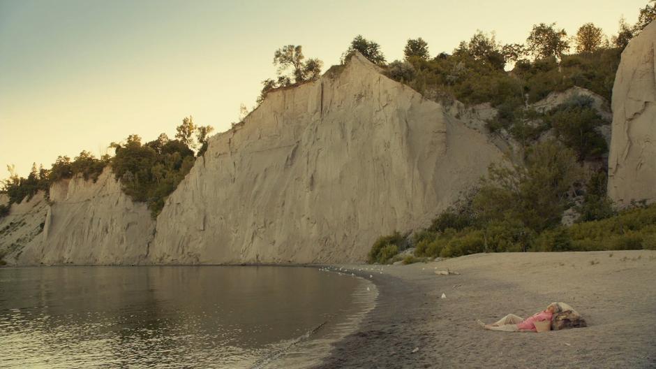 The woman lies dead on the beach as the sun sets.