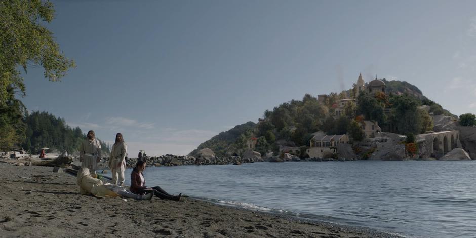 Sophie asks what is going on while sitting next to Alice on the beach while two guards watch over them.