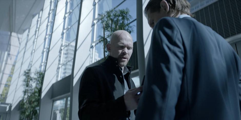 Victor Zsasz looks at the badge of a Hamilton employee in the lobby.