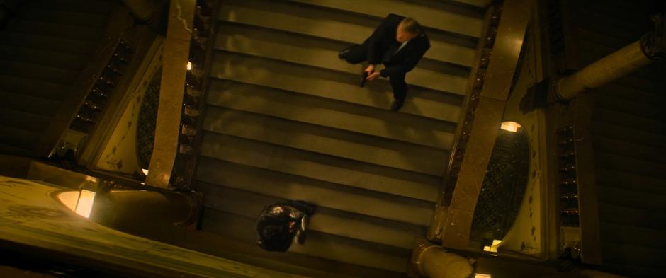 Bucky uses his arm to block bullets from a guard on the stairs.