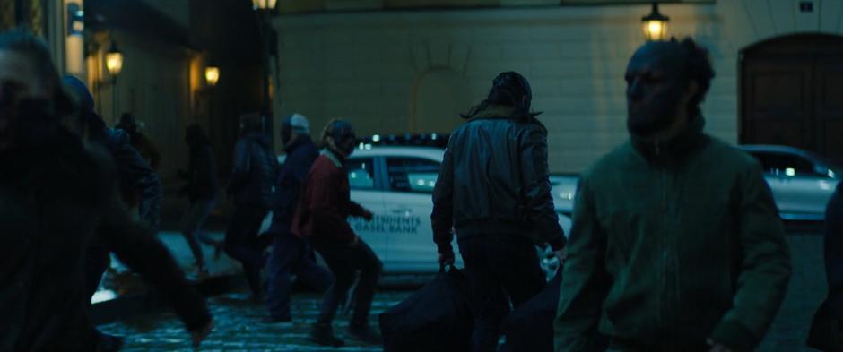 A masked member of the Flag Smashers walks through the crowd with the two bags.