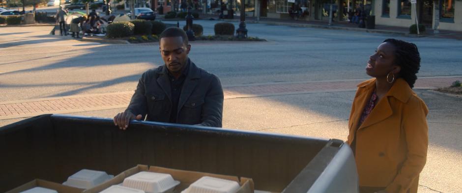 Sarah talks to Sam as he opens the bed of his pickup to get out the boxes of food.