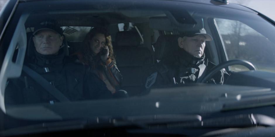 Angelique smiles at Ryan during their phone call while the two Crows Security guards drive her into witness protection.