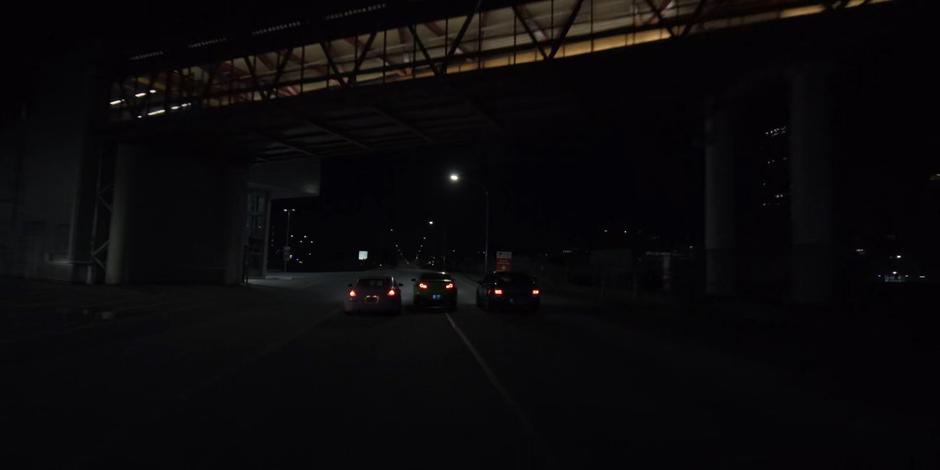 Three cars race beneath a pedestrian bridge.