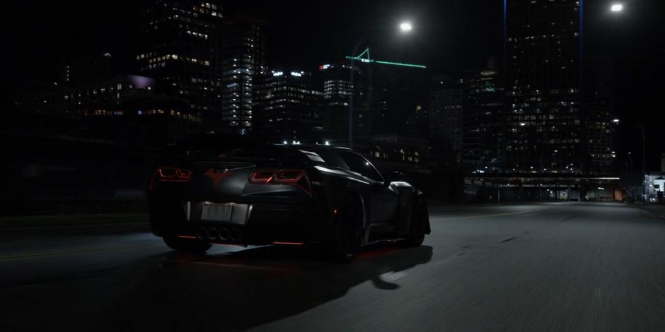 The Batmobile speeds along the waterfront at night.
