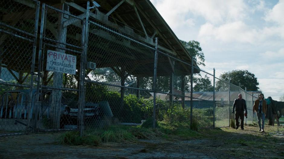 Mick and Behrad walk along the fence to the gate leading into the compound.