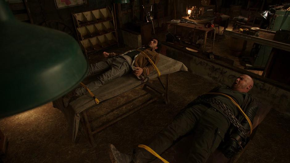 Behrad and Mick wake up and find themselves tied to two tables.