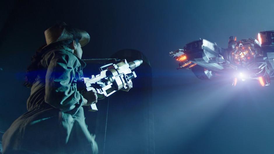 Spooner aims her giant gun at the Waverider as it shines a light down at her.
