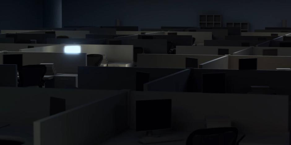 A long row of empty cubicles sit in the darkened room.