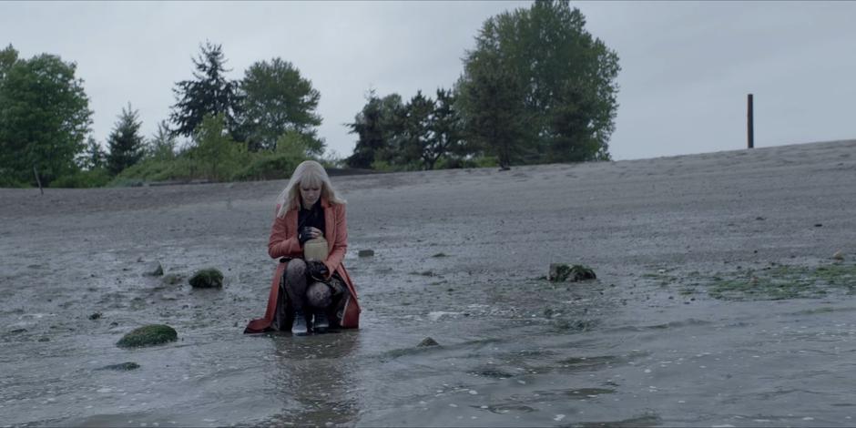 Alice kneels down at the waterline with Ocean's ashes.