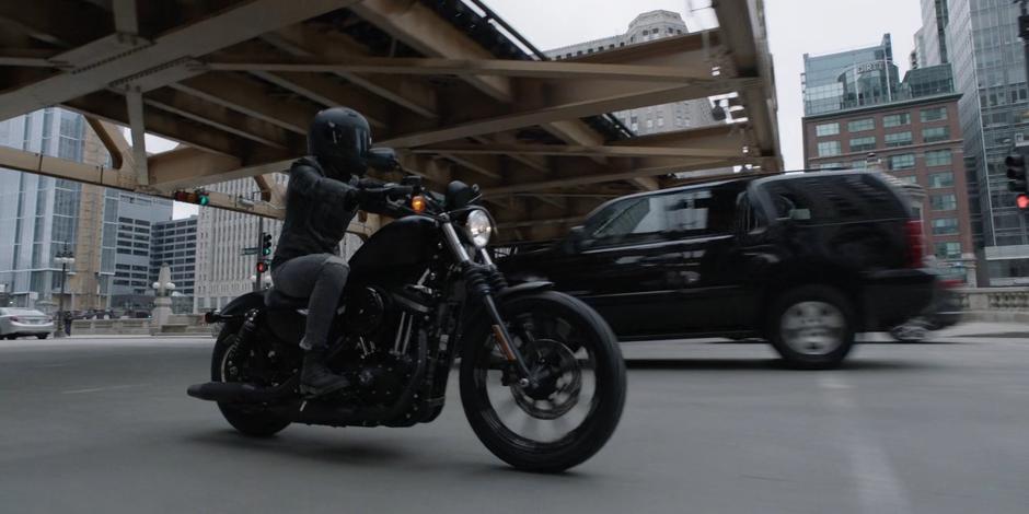 Kate rides her motorcycle beneath a set of elevated tracks.