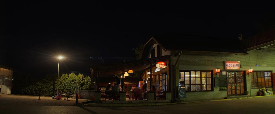 Natasha and Yelena sit down at a table outside the coffee shop attached to the gas station.