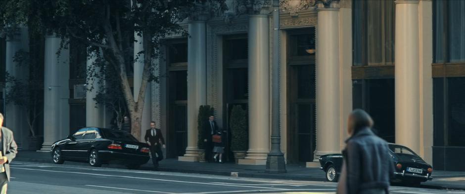 A guard holds the door open for Antonia while her driver runs back around his car.