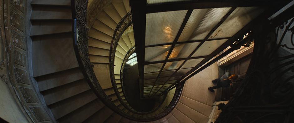 Natasha stands at the door to the side of the spiral stairscase and picks the lock to the safe house.