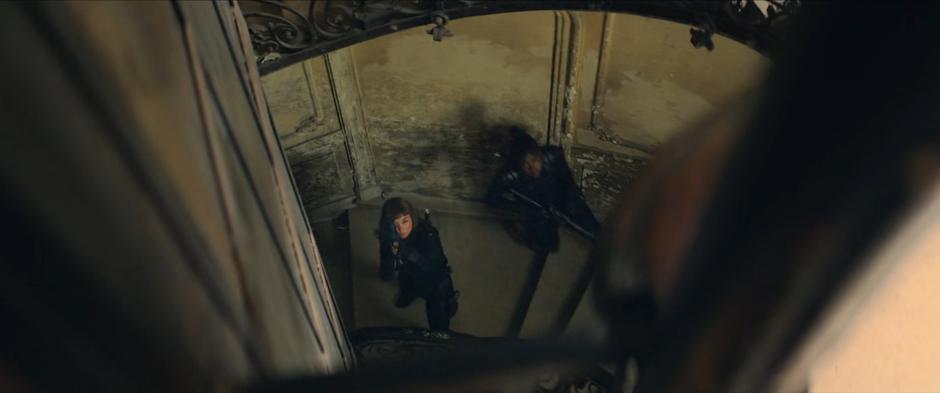 Two Widows coming up the stairs stop and take aim at Yelena.