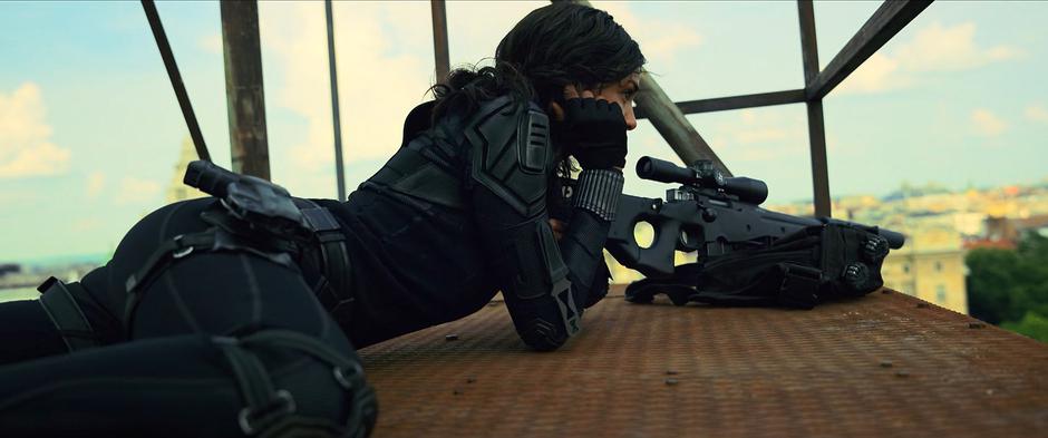 Ingrid listens to her coms from her sniper perch on a building adjacent to the safe house.