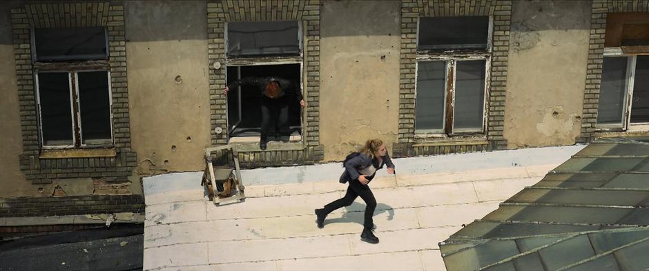 Natasha and Yelena exit through a window and run across the rooftop.