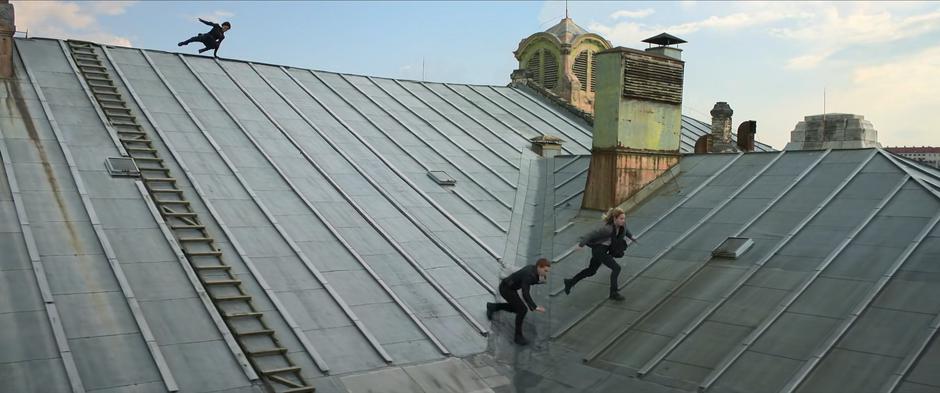 Natasha and Yelena run across the roof as Ingrid leaps over the peak behind them.