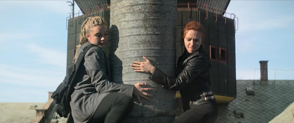 Yelena and Natasha push off from the roof as they hang on to the chimney.