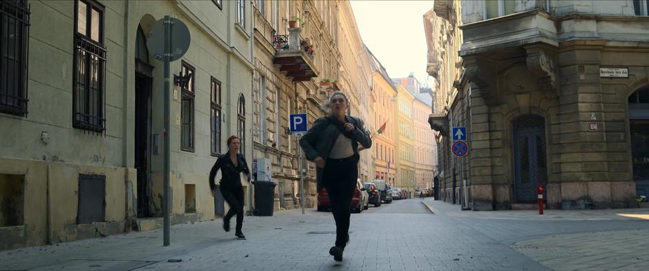 Natasha and Yelena run out of the building and down the street.