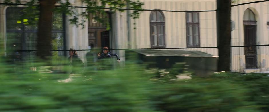 Yelena and Natasha run down the street past a park.