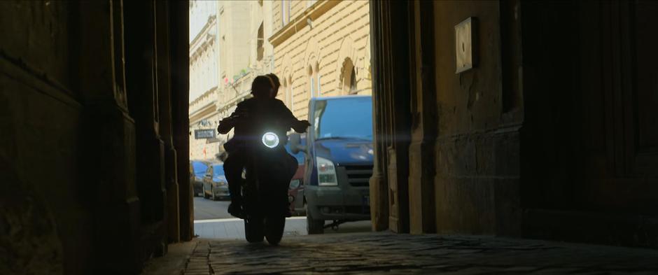 Natasha and Yelena ride the motorcycle down a pedestrian passage.