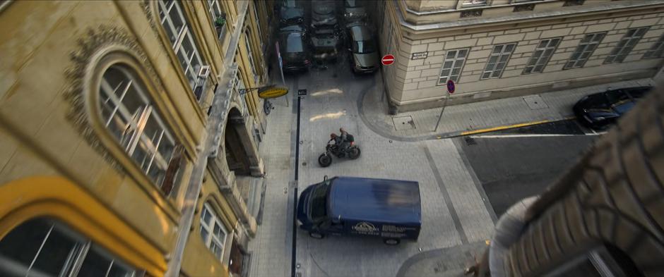 Natasha turns the motorcycle into a pedestrian passage as a truck pulls into their path and the armored vehicle approaches from behind.