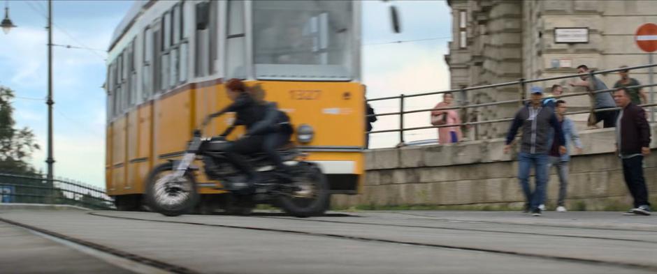 Natasha and Yelena ride just in front of a passing trolly.