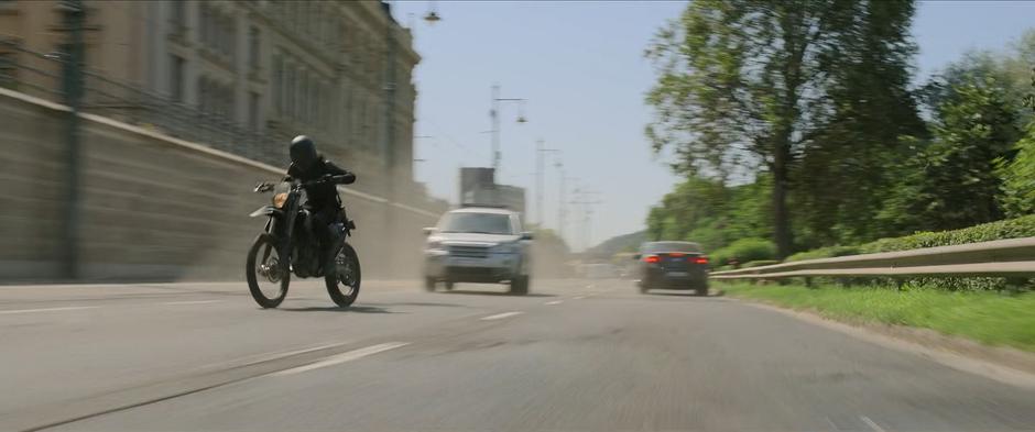 The pursuing Widow follows down the waterfront road on her motorcycle.