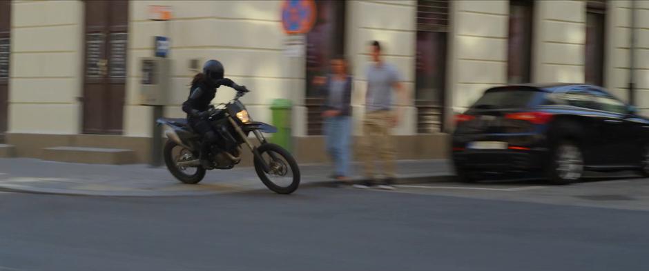 Two pedestrians jump back as the Widow rides her motorcycle through an intersection in front of them.