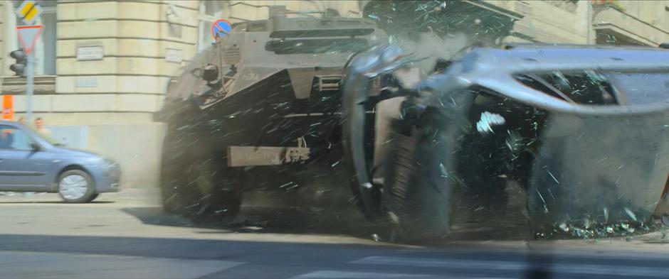 The armored vehicle smashes through a passing car as it rounds the corner.