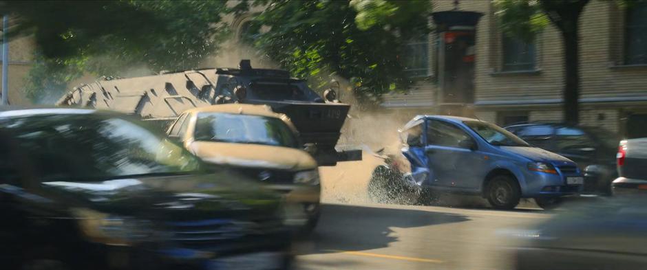 The armored truck smashes two cars to the side as it barrels down the street.