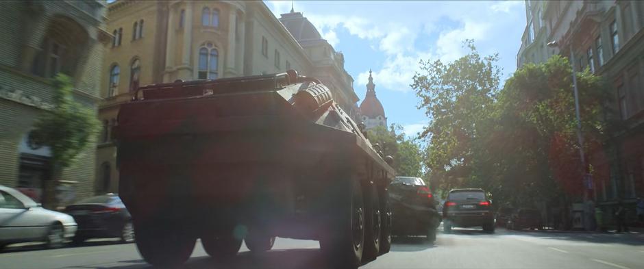 The armored truck smashes into another car as it drives down the street.