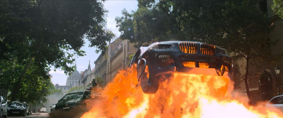 An explosion throws the stolen car into the air in front of Taskmaster's armored vehicle.