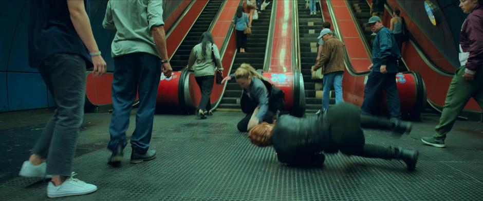 Yelena and Natasha roll on the ground at the bottom of the escalators after leaping to avoid the shield.